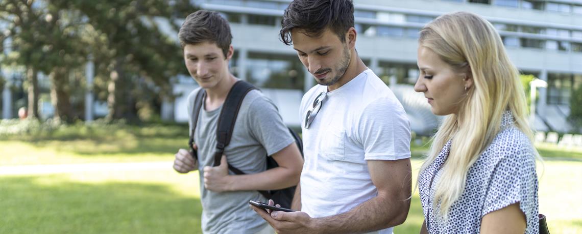 Studierende laufen über den THU-Campus und schauen auf ein Handy. 